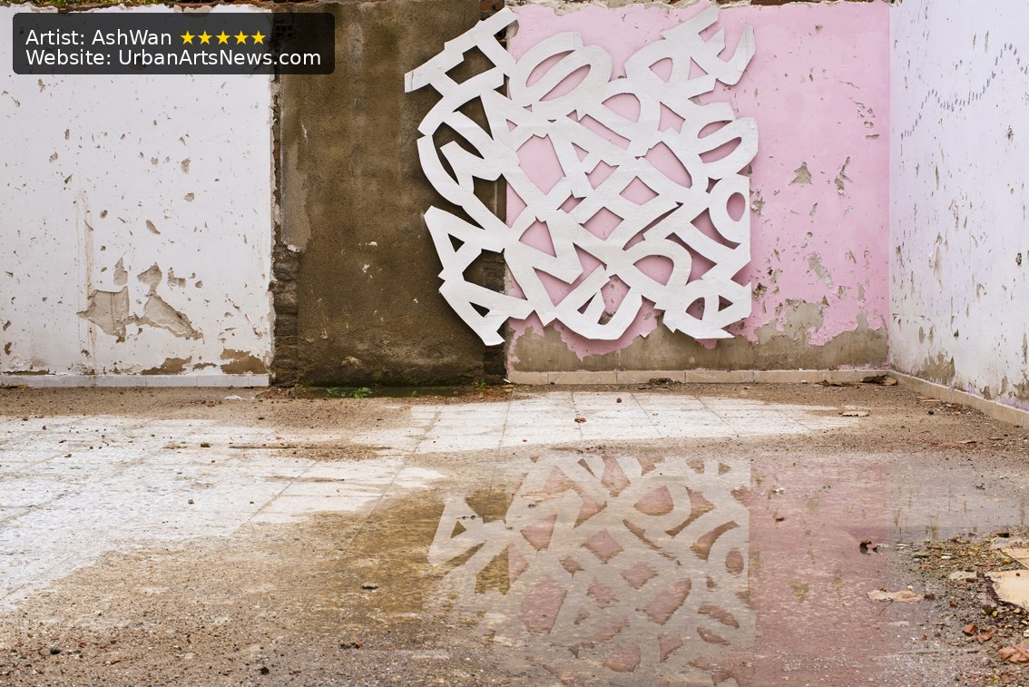 A white abstract letter installation by AshWan reflected in a rain puddle in an urban Barcelona setting.